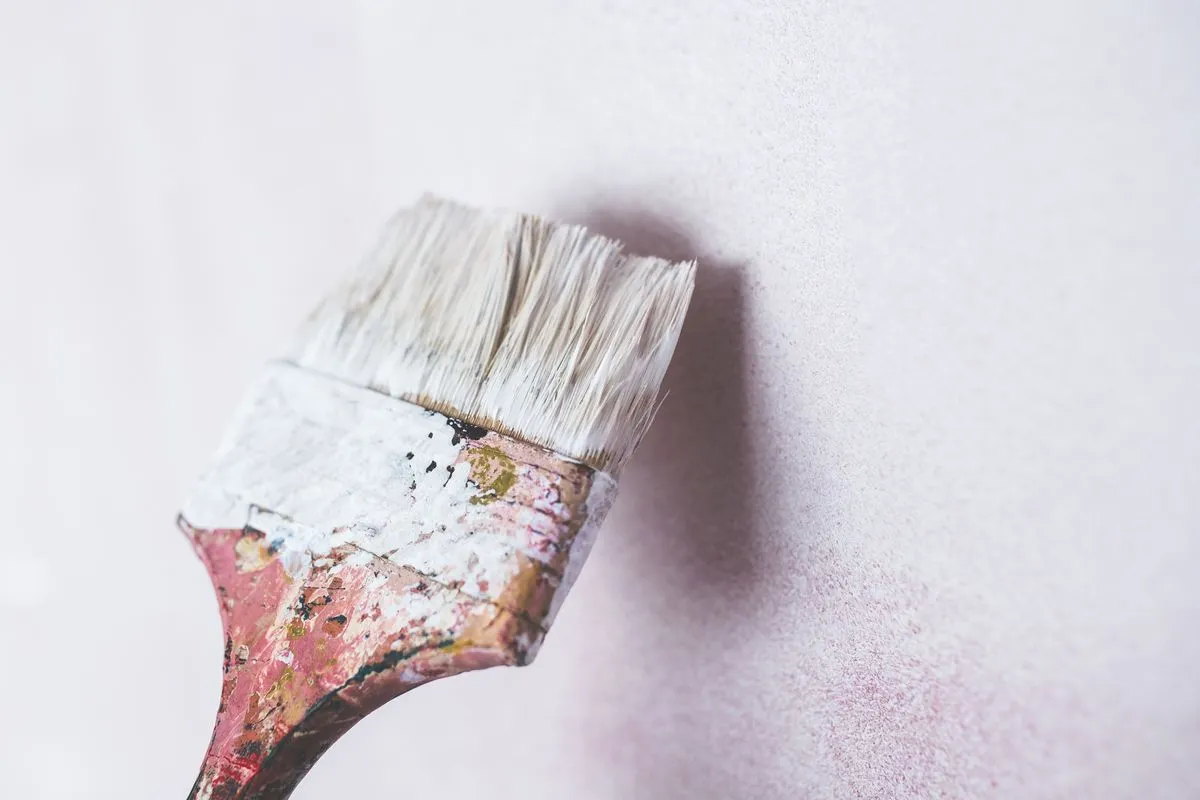 Gros plan d’un pinceau appliquant de la peinture blanche sur un mur.